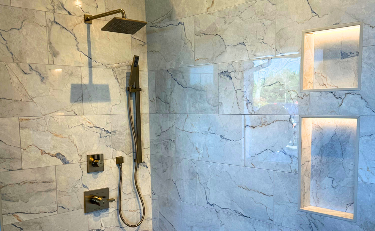 Custom walk-in tiled shower with gold hardware and wall enclave