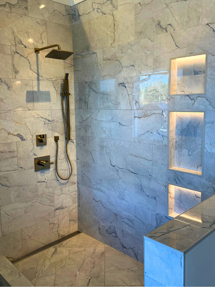Custom walk-in tiled shower with gold hardware and wall enclave